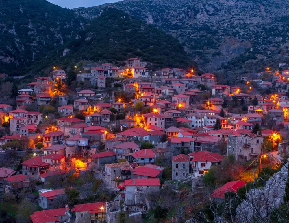 Η Στεμνίτσα, φωτισμένη το σούρουπο, με τα παραδοσιακά πέτρινα αρχοντικά και τις κόκκινες στέγες στα βουνά της Γορτυνίας.